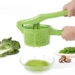 Exprimidor escurridor de cocina verde aplastando verduras para jugo fresco, con repollo y champiñones.