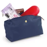 Bolso cartera azul marino plegable con cosmetiquera transparente de maquillaje y accesorio rojo.
