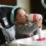 Porta teteros para bebés, niño usando tetero auto-soportable en silla de comer