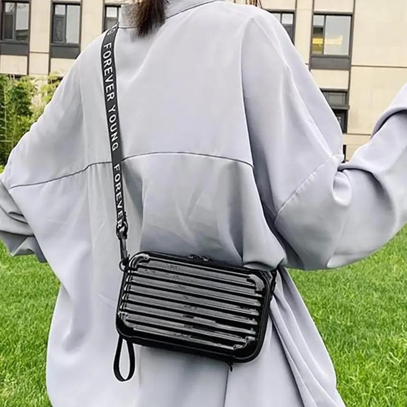 Mini bolso negro con correa de texto "Forever Young" cruzado sobre una chaqueta gris.