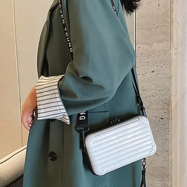 Mini bolso blanco tipo maleta con correa de tela con texto, estilo moderno.