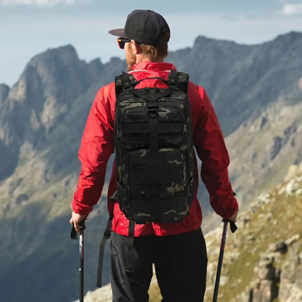 Bolso táctico deportivo militar camuflado que lleva un hombre en la montaña con bastones de senderismo.