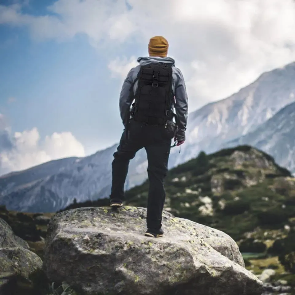 Persona con bolso táctico deportivo, explorando un paisaje montañoso con cielo azul y nubes.
