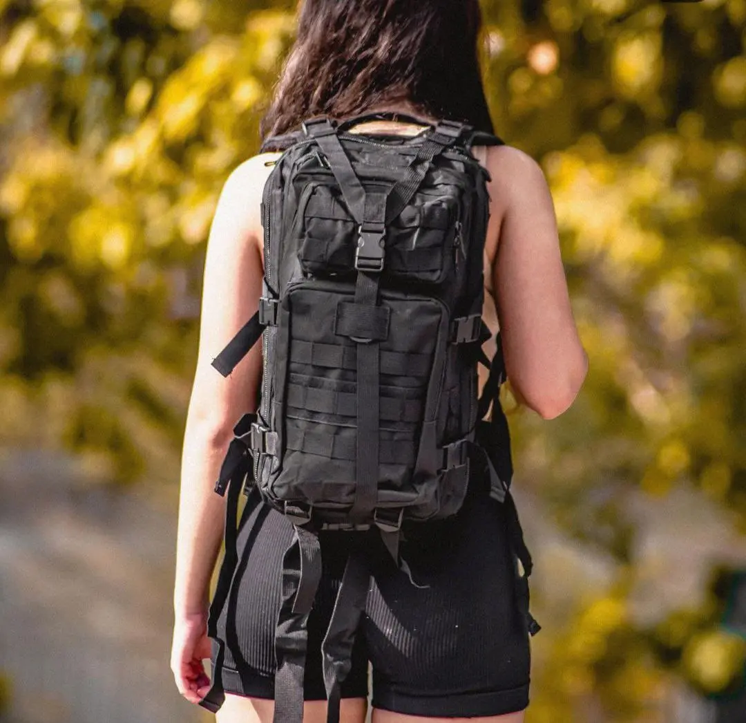 Mujer con bolso táctico deportivo negro para exteriores, con detalles de correas y compartimentos.
