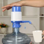 Bomba manual para dispensador de agua en botellón, extrayendo agua hacia una taza.