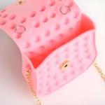 Bolso rosado para niña estilo pop it con cadena dorada y broche magnético.
