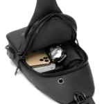 Bolso pechero negro con celular y reloj digital en su interior, diseño moderno.