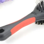 Cepillo para mascotas doble cara con mango ergonómico y hueco para colgar.