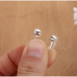 Clip nasal de sueño plateado para uso x2, sujetado por dedos humanos.