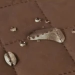Cubre sofá de 2 puestos marrón con gotas de agua visibles, textura acolchada.
