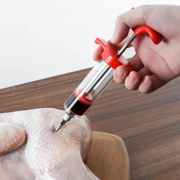 Inyector de carne con jeringa para marinar pollo crudo en mesa de madera.