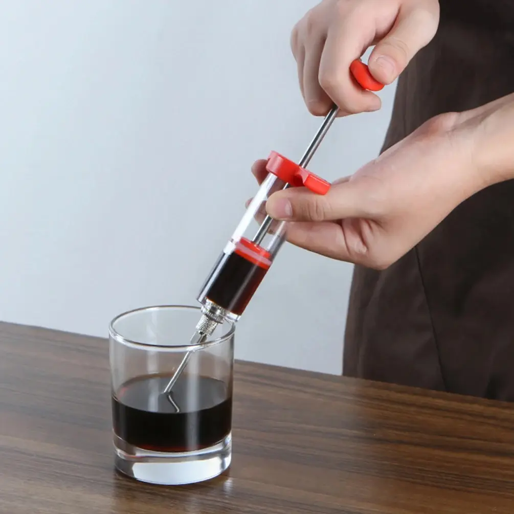 Inyector de carne de acero inoxidable recogiendo líquido de un vaso.
