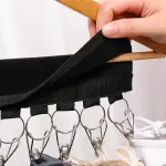 Organizador de gorras negro colgado en una percha de madera con pinzas plateadas.