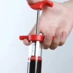 Inyector de carne con émbolo rojo y líquido oscuro, sostenido por una mano.