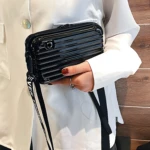 Mini bolso negro con correa de texto blanco, estilo maleta, sostenido por una mano con anillo.