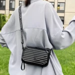 Mini bolso negro tipo maleta con correa "Forever Young" colgado en un outfit blanco.