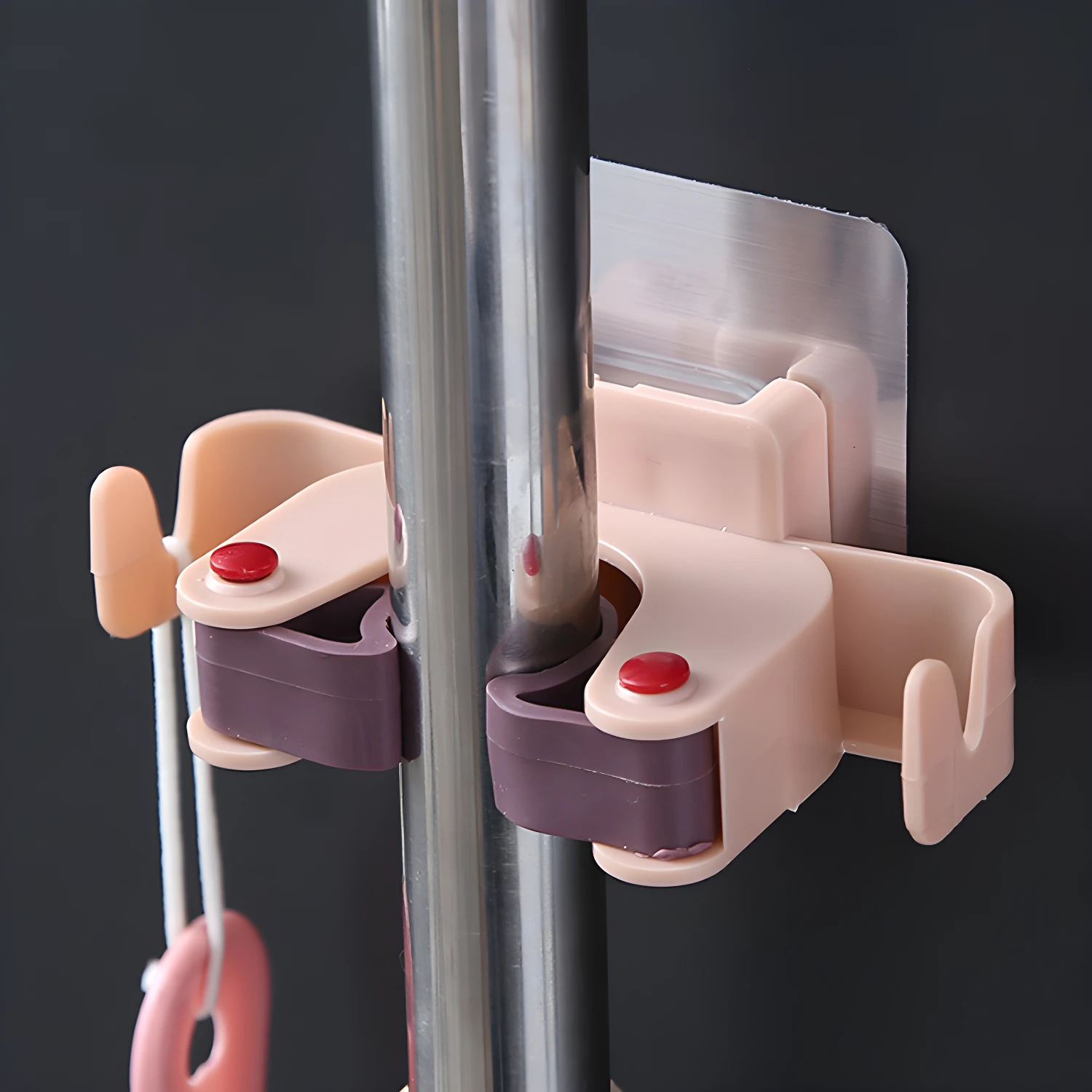 Set x2 soportes adhesivos para escobas y traperos, con gancho de plástico rosado.