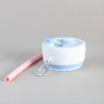 Taza de café plegable de silicona blanca con pajilla rosa y mosquetón, ideal para viajes.