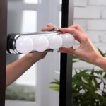 Tira de 4 bombillos LED Studio Glow para espejo de tocador, manos instalando luz.