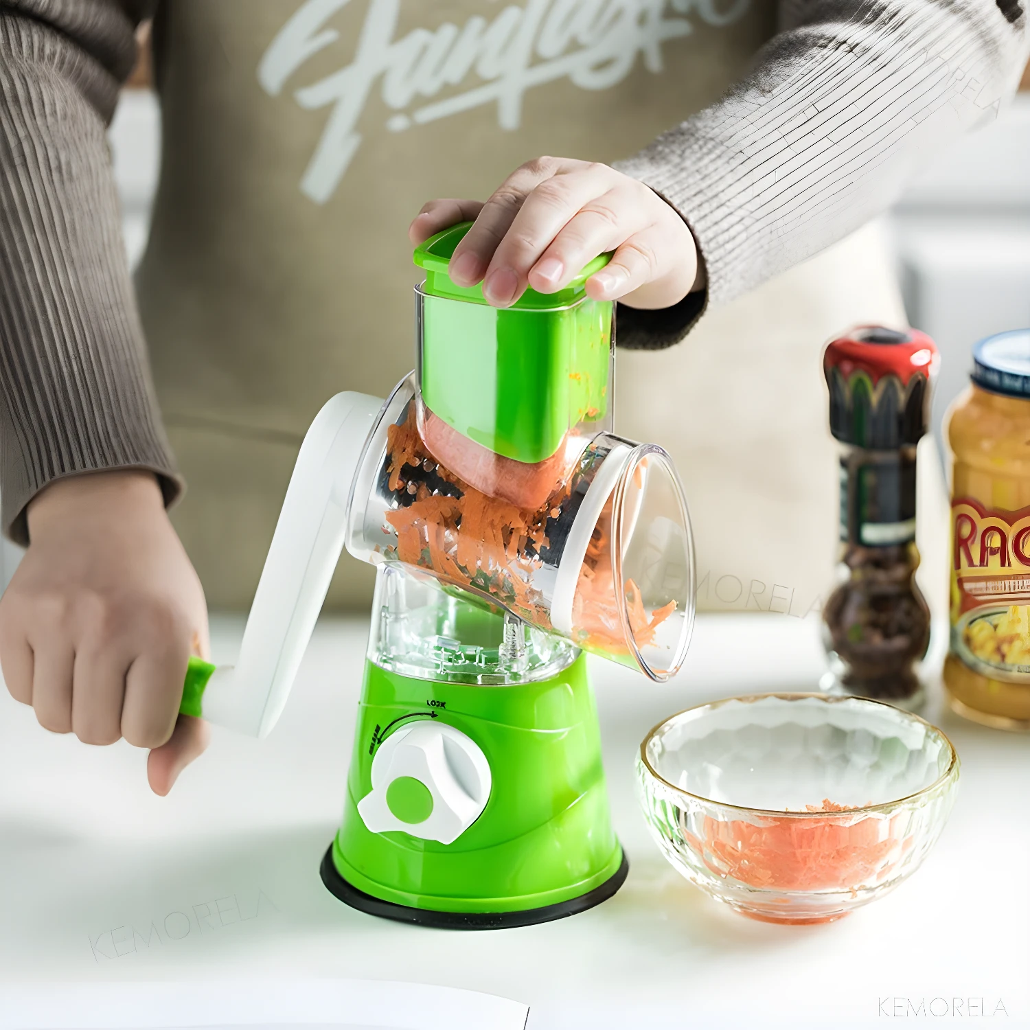 Rallador molino de verduras giratorio verde con base de succión rallando zanahoria en tazón.