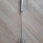 Batidor manual de acero inoxidable con alambre en forma de globo sobre fondo de madera.