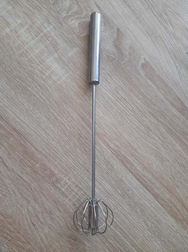Batidor manual de acero inoxidable con alambre en forma de globo sobre fondo de madera.
