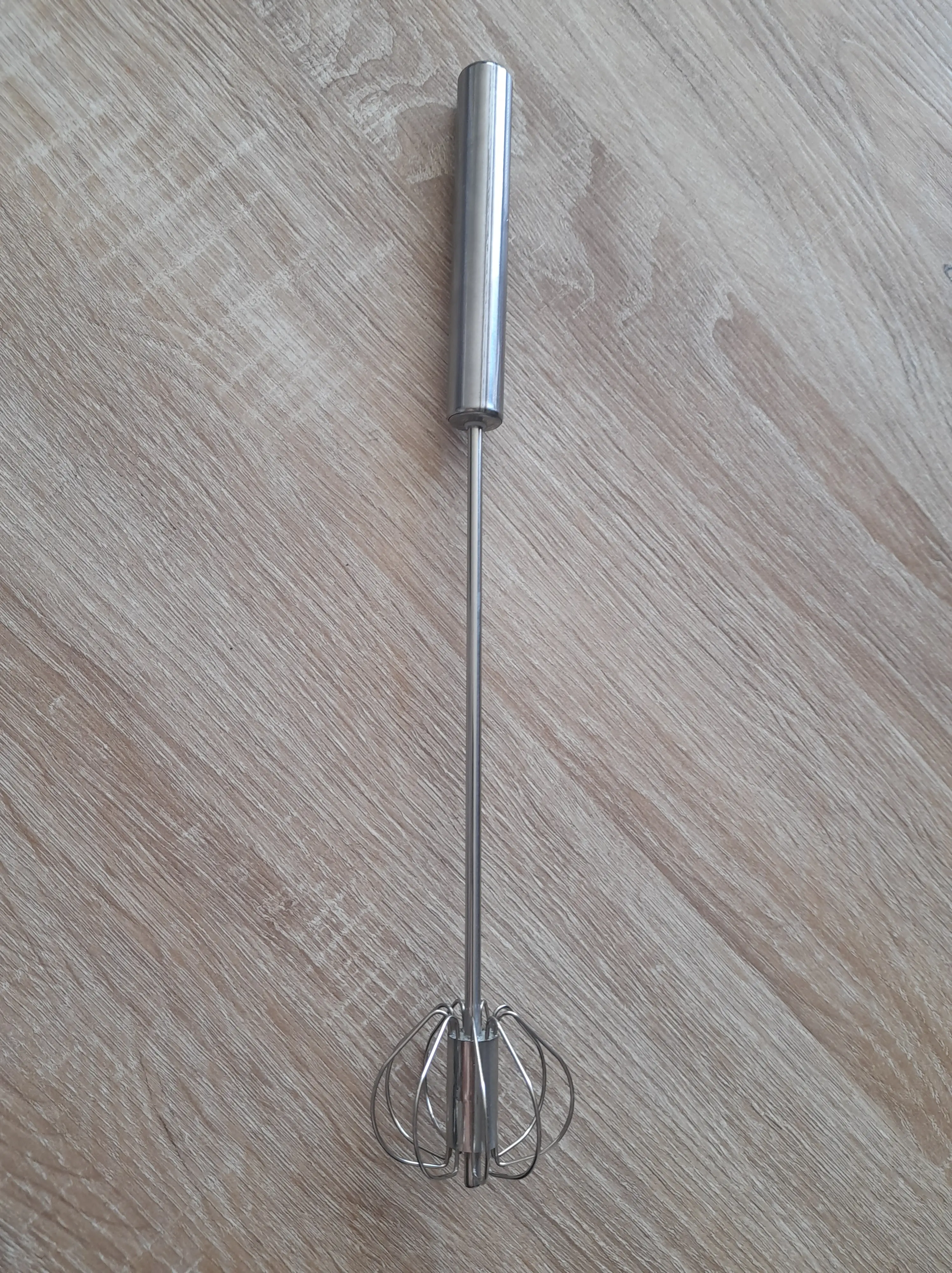 Batidor manual de acero inoxidable con alambre en forma de globo sobre fondo de madera.