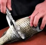 Persona usando cuchillo para quitar escamas de pescado crudo fresco.
