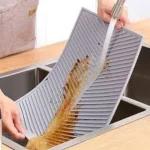 Tapete de cocina multifuncional gris inclinado sobre el lavaplatos, con agua lavando restos de comida.