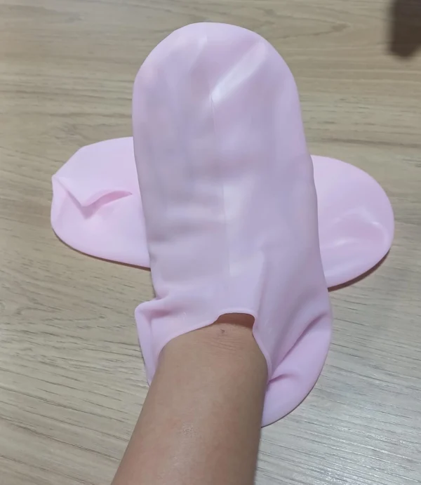 Medias spa hidratantes de silicona rosa cubriendo un pie y tobillo sobre superficie de madera.