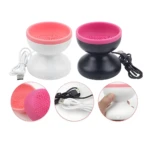 Limpiador de brochas eléctrico blanco y negro con detalles de carga y texturas de silicona.