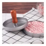 Molde para hamburguesas de carne con prensa de madera sobre fondo a cuadros.