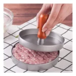Molde para carne de hamburguesa con prensa de madera aplastando carne picada en forma circular.