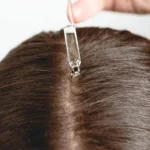 Suero Ordinary con pipeta aplicando gotas en la raíz del cabello oscuro para densidad.