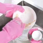 Guantes de silicona rosa con cerdas integradas para lavar platos y vajilla en el lavaplatos.