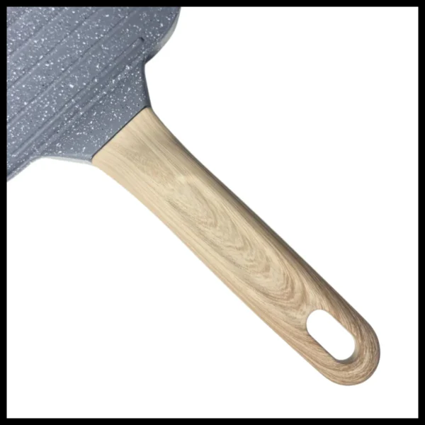 Sartén en forma de corazón gris con mango de madera claro, vista de cerca.