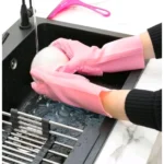 Guantes de silicona rosa con esponja incorporada para lavar platos en el fregadero, con escurridor metálico.