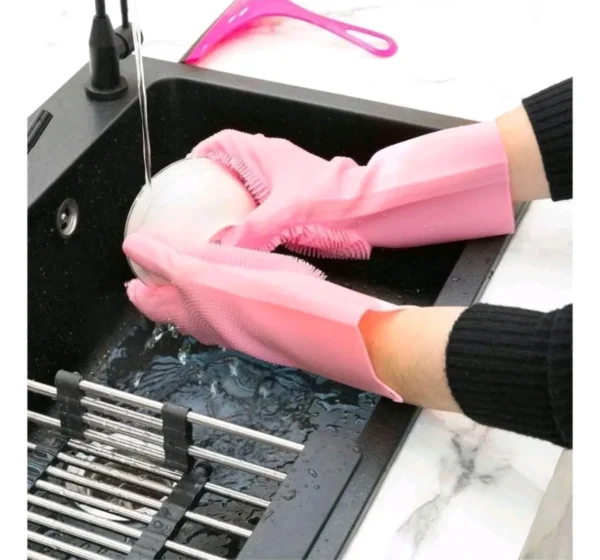Guantes de silicona rosa con esponja incorporada para lavar platos en el fregadero, con escurridor metálico.