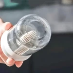 Dispensador de aceite transparente con cuchillas, sostenido en mano.