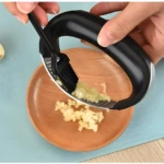 Picador de ajos ergonómico de acero inoxidable triturando ajos sobre plato de madera.