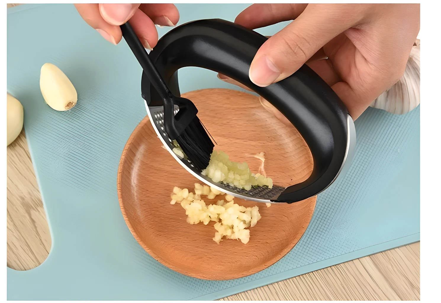Picador de ajos ergonómico de acero inoxidable triturando ajos sobre plato de madera.