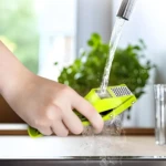 Picador triturador de ajo verde siendo enjuagado bajo el grifo en una cocina luminosa.