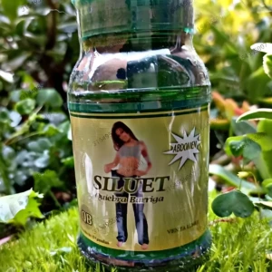 Bote de Siluet Quiebra Barriga quemador de grasa con etiqueta dorada y figura de mujer, en césped verde.