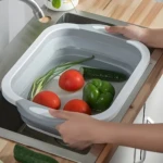 Tabla multifuncional con escurridor lavando verduras frescas en un fregadero.