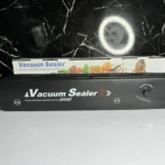 Selladora al vacío Vacuum Sealer Z negra con bolsa, perfecta para empacar alimentos.