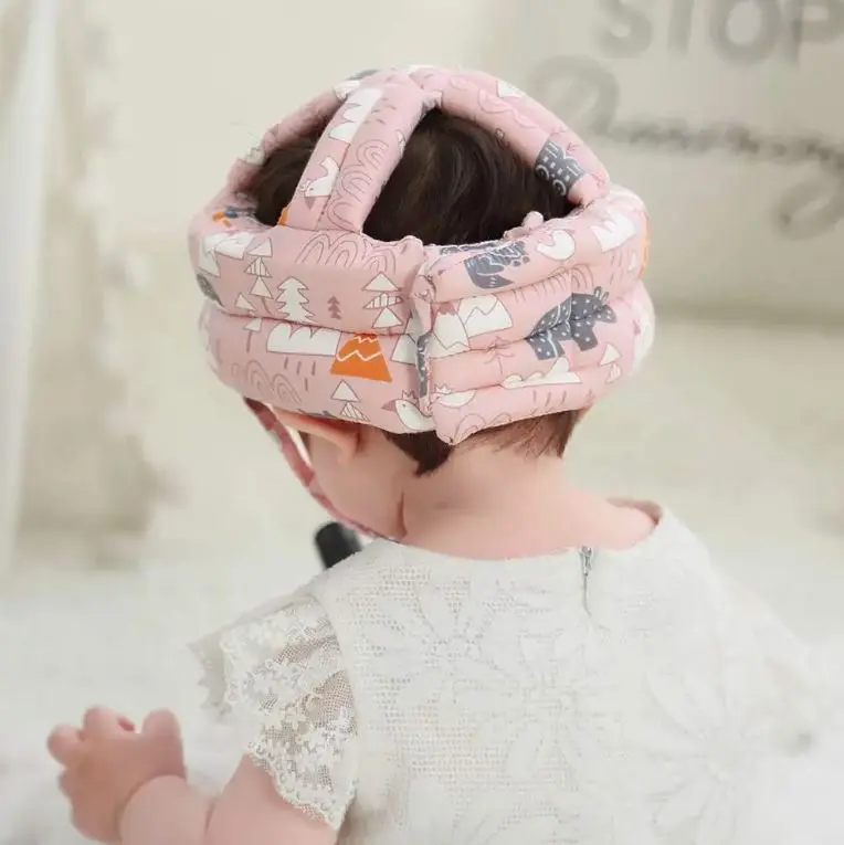 Bebé con casco protector rosa con estampado de animales y montañas, visto desde atrás.