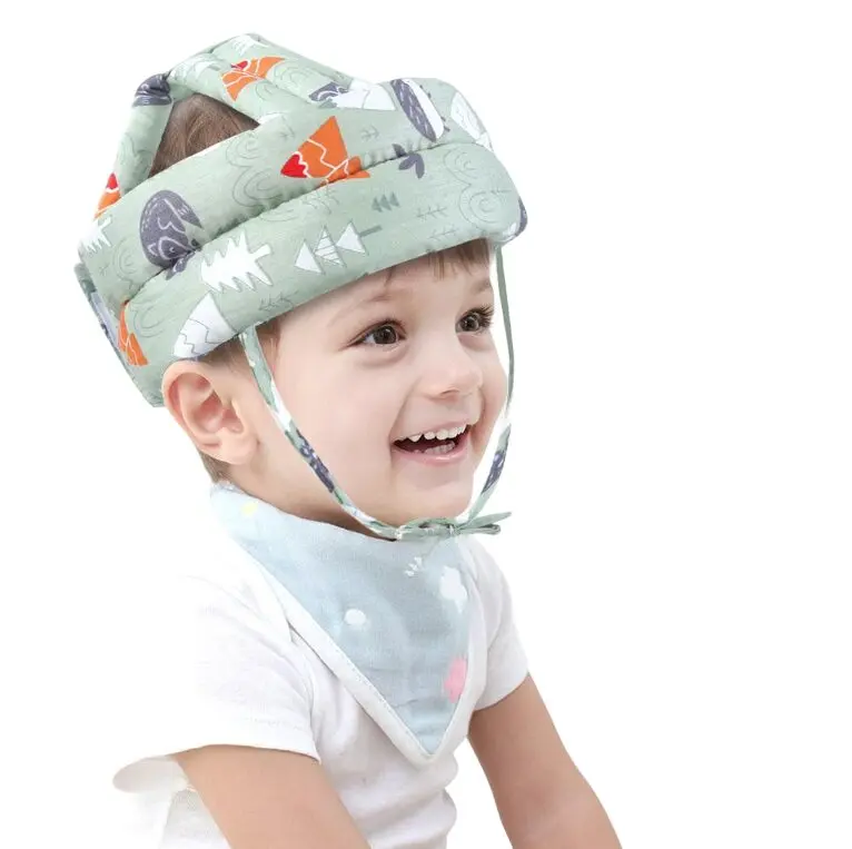 Bebé sonriente con protector de cabeza con estampado de árboles y ardillas.