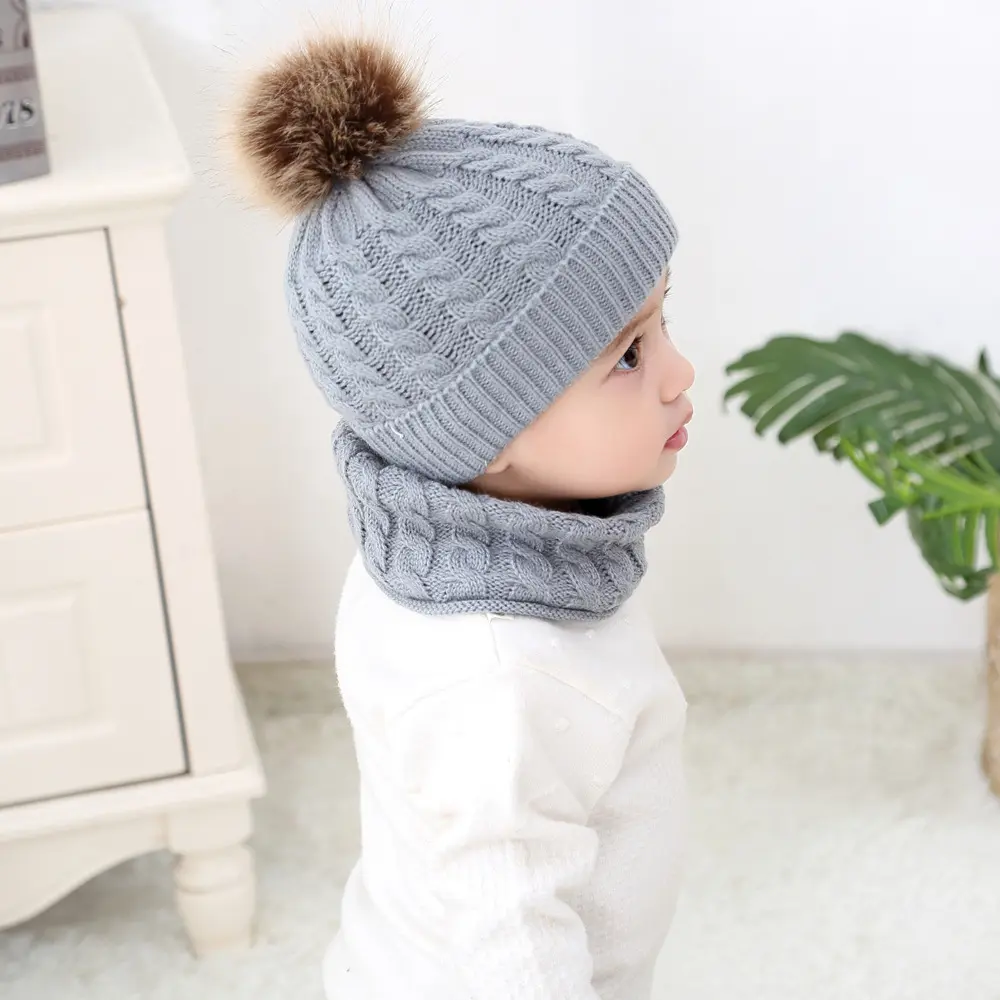 Gorro y bufanda tejidos de lana gris para bebé con pompón marrón y textura de trenza.