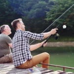 Kit Caña De Pescar con Anzuelos y Señuelos para Carrete, dos hombres pescando en muelle.