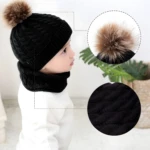 Gorro y bufanda negros tejidos para bebé con pompón de pelo y textura suave.